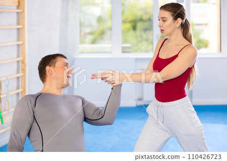 Young woman learns to do painful grip on arm of an attacking man during self defense training Young woman learns to do painful grip on arm of an attacking man during self defense training 110426723