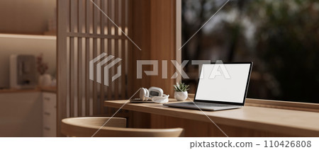 A white-screen laptop mockup on a wooden table against the window in a modern, comfortable room. 110426808