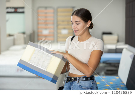 Girl chooses mattress filling in furniture store 110426889