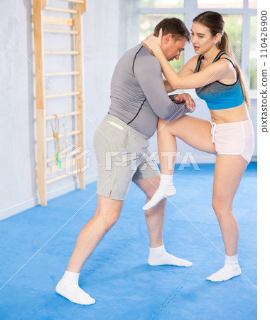 Young girl practicing feet kick method of self-defense in pair with middle-aged man Young girl practicing feet kick method of self-defense in pair with middle-aged man 110426900