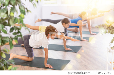 Friendly sporty parents with tween daughter and son performing Balancing Table Pose on gymnastic mats barefoot in yoga studio 110427059