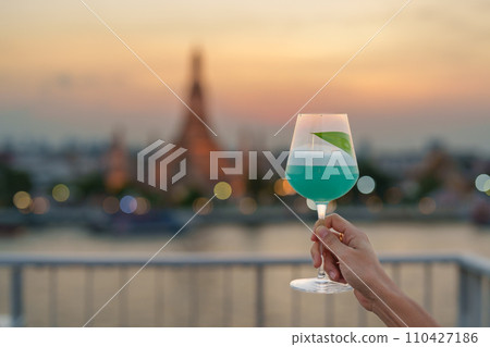 tourist hand shows cocktail glass during enjoy view to Wat Arun Temple in sunset, Traveler visits Temple of Dawn near from rooftop bar. Travel destination in Bangkok, Thailand and Southeast Asia tourist hand shows cocktail glass during enjoy view to Wat Arun Temple in sunset, Traveler visits Temple of Dawn near from rooftop bar. Travel destination in Bangkok, Thailand and Southeast Asia 110427186