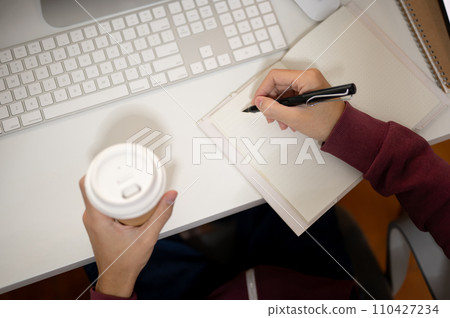 Top view image of an office man taking notes in a book and sipping coffee at his office desk. 110427234