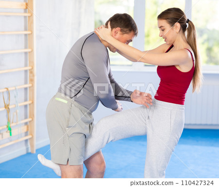 Young girl practicing feet kick method of self-defense in pair with middle-aged man Young girl practicing feet kick method of self-defense in pair with middle-aged man 110427324