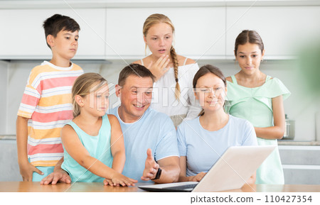 Large family is sitting in kitchen next to laptop and making video call to grandparents 110427354