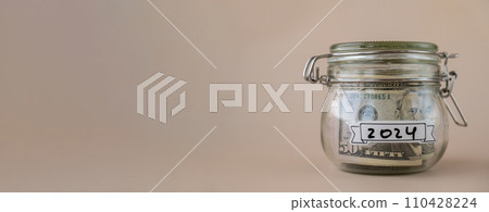 Glass jar full of American currency dollars cash banknote with text 2024 year. Preparation saving money. Moderate consumption and economy Glass jar full of American currency dollars cash banknote with text 2024 year. Preparation saving money. Moderate consumption and economy 110428224