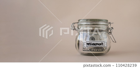 Glass jar full of American currency dollars cash banknote with text RETIREMENT. Preparation saving money. Moderate consumption and economy Glass jar full of American currency dollars cash banknote with text RETIREMENT. Preparation saving money. Moderate consumption and economy 110428239