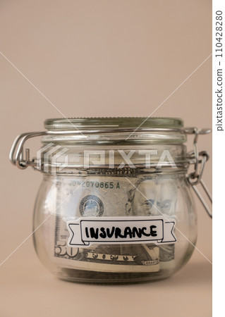Saving Money In Glass Jar filled with Dollars banknotes. INSURANCE transcription in front of jar. Managing personal finances extra income for future insecurity Saving Money In Glass Jar filled with Dollars banknotes. INSURANCE transcription in front of jar. Managing personal finances extra income for future insecurity 110428280