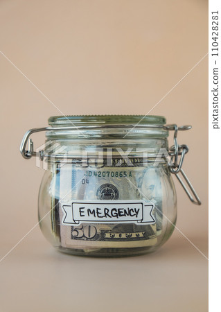 Glass jar full of American currency dollars cash banknote with text EMERGENCY. Preparation saving money. Moderate consumption and economy Glass jar full of American currency dollars cash banknote with text EMERGENCY. Preparation saving money. Moderate consumption and economy 110428281