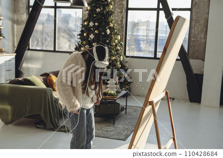 In a Christmas setting, a young woman in light clothing and a virtual reality headset stands in front of the mirror. In a Christmas setting, a young woman in light clothing and a virtual reality headset stands in front of the mirror. 110428684