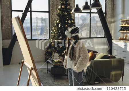 On a sunny day, a vibrant young lady wears a virtual reality headset before the mirror. 110428715