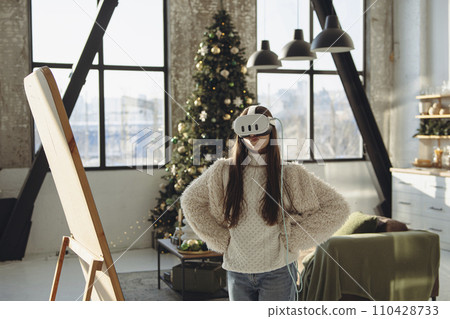 With a Christmas tree as a backdrop, a lovely young lady engages in virtual reality. 110428733
