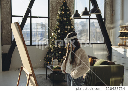 Engrossed in virtual reality, a bright young woman stands before a mirror on a sunny day. 110428734