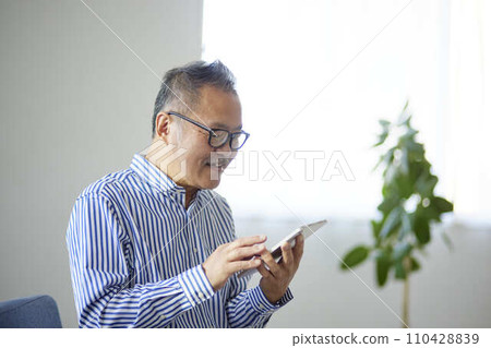 Japanese senior man using a tablet device in the living room Japanese senior man using a tablet device in the living room 110428839