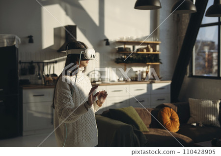 In the comfort of her apartment, a stunning young lady plays an online game with a VR headset. 110428905