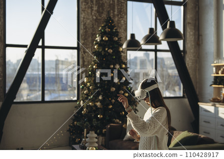 In her apartment, a beautiful young lady enjoys gaming online with a virtual reality headset. 110428917