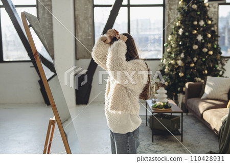 In a joyful moment, a lively young woman wearing a Christmas reindeer mask smiles brightly at home. In a joyful moment, a lively young woman wearing a Christmas reindeer mask smiles brightly at home. 110428931