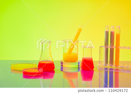 Colorful liquids are contained in test tubes, petri dishes, beakers and Erlenmeyer flasks on a green-yellow gradient background. Inside the laboratory. 110429172