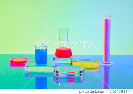 Red, pink, yellow and blue liquids inside glassware and transparent platforms on a green-blue gradient background. Lab space for advertising. 110429174