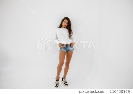 Beautiful girl in shorts and a white sweatshirt posing on a white background 110430569