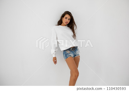 Beautiful girl in shorts and a white sweatshirt posing on a white background 110430593