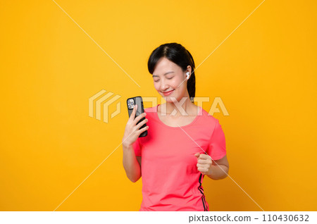 Portrait young asian sports fitness woman happy smile wearing pink sportswear and smartphone doing exercise training workout against yellow studio background. technology wellness lifestyle concept. 110430632
