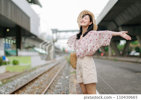 young asian woman traveler with weaving basket happy smiling looking to a camera beside train railway. Journey trip lifestyle, world travel explorer or Asia summer tourism concept. 110430665