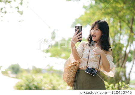 Portrait of asian young woman traveler with weaving hat, basket, mobile phone and camera on green public park background. Journey trip lifestyle, world travel explorer or Asia summer tourism concept. 110430746