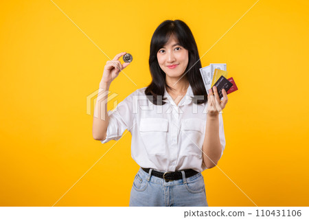 Capture the essence of digital currency with stunning portrait of young Asian woman confidently holds digital currency, cash, credit card, and smartphone. The digital currency concept. 110431106