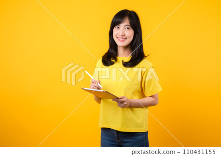 Experience the joy of education technology with portrait. A young Asian woman wearing a yellow t-shirt and denim jeans showcases a happy smile while using digital tablet. education technology concept. Experience the joy of education technology with portrait. A young Asian woman wearing a yellow t-shirt and denim jeans showcases a happy smile while using digital tablet. education technology concept. 110431155