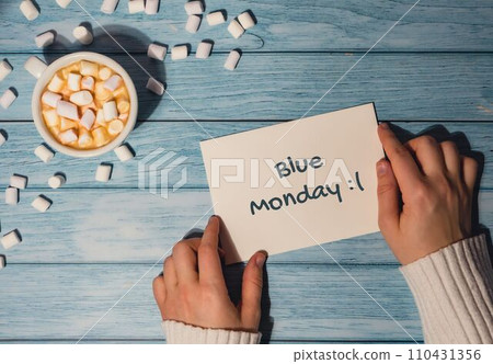 BLUE MONDAY concept text Female hands holding card with white cup of coffee and marshmallows on wooden background. The most depressing day of the year in January. Day commit suicide and depression BLUE MONDAY concept text Female hands holding card with white cup of coffee and marshmallows on wooden background. The most depressing day of the year in January. Day commit suicide and depression 110431356