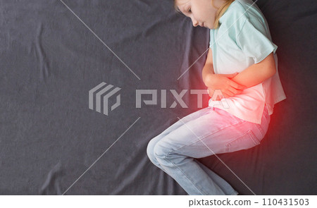 A little caucasian girl of seven years old is lying on the bed with her legs crossed and holding her red belly. Concept of abdominal pain due to poisoning, rotavirus infection. Indigestion, bloating 110431503