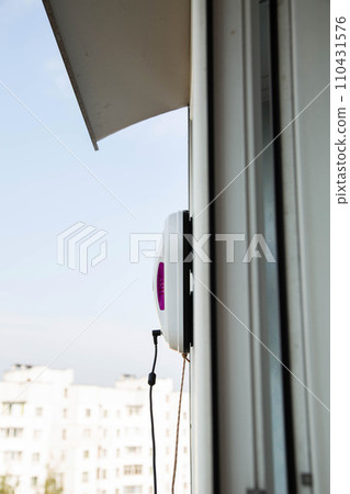 A modern vacuum robot window washer washes glass in an apartment on a balcony. View outside from the street. Safety from falls from a height. 110431576
