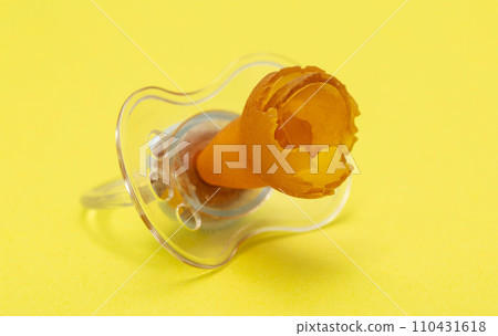 A chewed baby pacifier on a yellow background. Concept of teething in children, close-up. 110431618