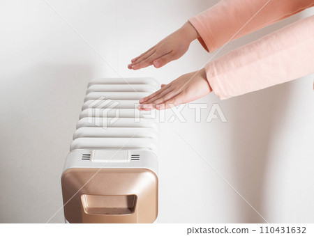 Children's hands on the background of an oil electric heater on a white background. Concept for turning on heating in apartments, temperature in the house. 110431632