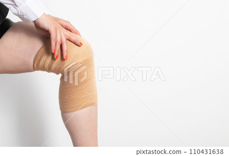 The girl puts on an elastic orthopedic knee pad on a sore leg. Arthrosis and knee injury. Fixation of the knee joint. Copy space for text The girl puts on an elastic orthopedic knee pad on a sore leg. Arthrosis and knee injury. Fixation of the knee joint. Copy space for text 110431638