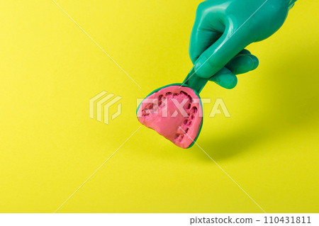 The hand of a dentist doctor in a green medical glove holds a dental spoon with an alginate plastic mass for making a plaster cast of the patient s jaw on a yellow background. Concept of malocclusion 110431811