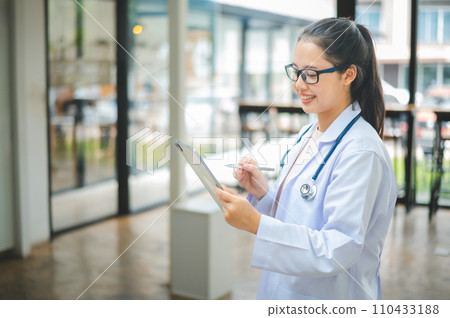 Portrait doctor with a stethoscope and using digital tablet stands confidently ready for healthcare visitor in hospital or clinic. 110433188