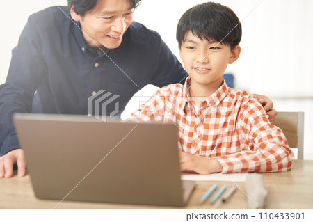 Elementary school boy studying while looking at a computer and a man watching over him 110433901