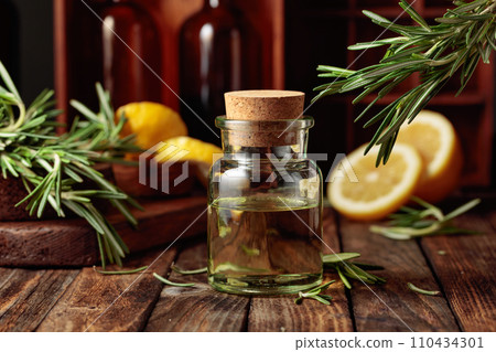 Bottle of essential oil, rosemary, and lemon on a wooden table. 110434301