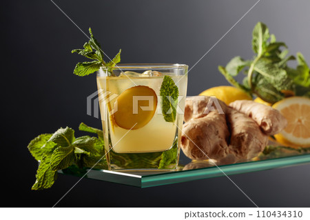 Ginger ale beer cocktail with lemon and mint in a frozen glass on a black background. Ginger ale beer cocktail with lemon and mint in a frozen glass on a black background. 110434310