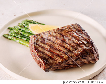 Grilled meat steak on plate with lemon and asparagus on white table background. Food and cuisine concept. 110434337