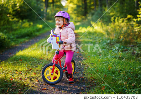 Child riding balance bike. Kids on bicycle in sunny forest. Little girl enjoying to ride glider bike on warm day. Preschooler learning to balance on run bicycle in safe helmet. Sport activity 110435708