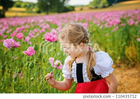 Little preschool girl in poppy field. Cute happy child in red riding hood dress play outdoor on blossom flowering meadow with pink poppies. Leisure activity in nature with children. Little preschool girl in poppy field. Cute happy child in red riding hood dress play outdoor on blossom flowering meadow with pink poppies. Leisure activity in nature with children. 110435712