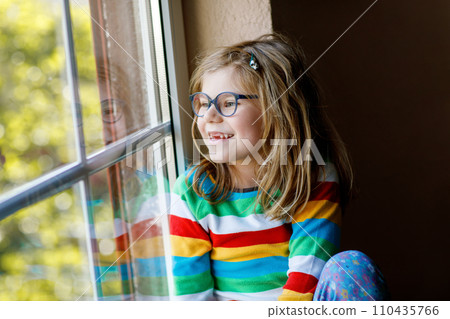 Adorable little preschool girl with eyeglasses sitting by the window. Thoughtful child looking out. Lonely kid. Adorable little preschool girl with eyeglasses sitting by the window. Thoughtful child looking out. Lonely kid. 110435766
