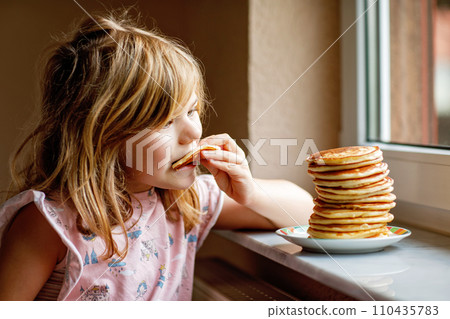 Little happy preschool girl with a large stack of pancakes for breakfast. Positive child eating healthy homemade food in the morning. Little happy preschool girl with a large stack of pancakes for breakfast. Positive child eating healthy homemade food in the morning. 110435783