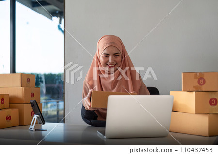 Muslim women selling online at home with box. Selling online with box to accept order from customer. Live stream selling online. muslim woman working smartphone and laptop at home Muslim women selling online at home with box. Selling online with box to accept order from customer. Live stream selling online. muslim woman working smartphone and laptop at home 110437453