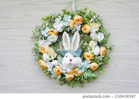 Easter wreath with bunny and flowers hanging on wooden door, close up 110438597