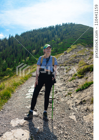Rear view of a young woman standing at the edge of a cliff overlooking high mountains. woman looking out over an idyllic mountain scene 110441159