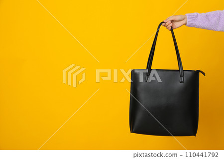 Black bag in hand on yellow background 110441792